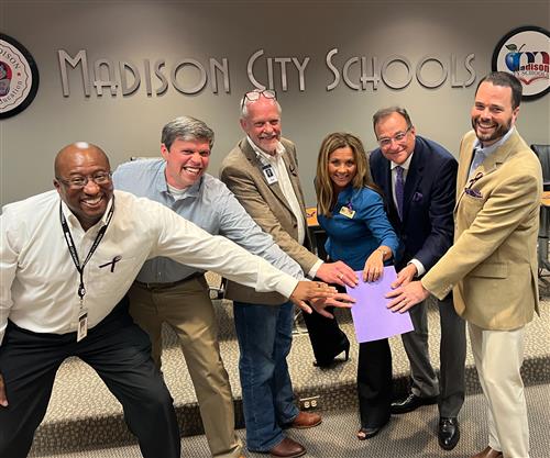 board members and dr. Nichols huddle around a paper giving a high five